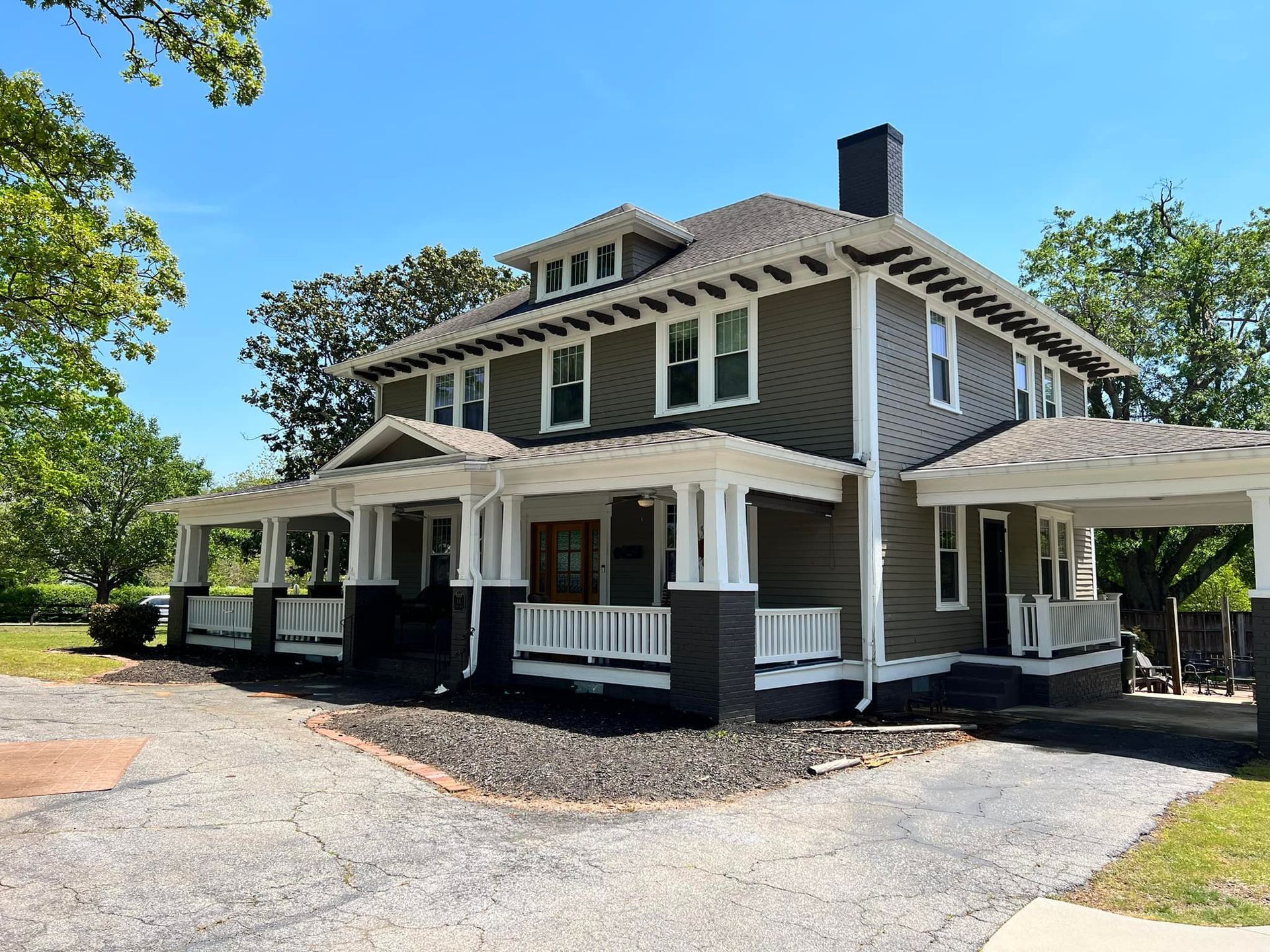 Two-story house with gray siding, white trim, and a porch under a blue sky.