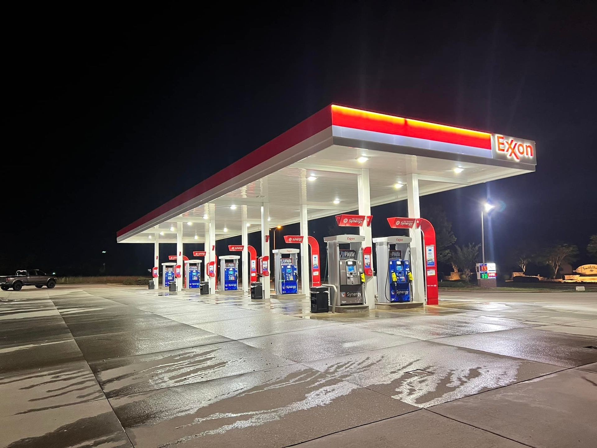 Gas station with red and white Exxon canopy at night, wet ground reflecting lights.