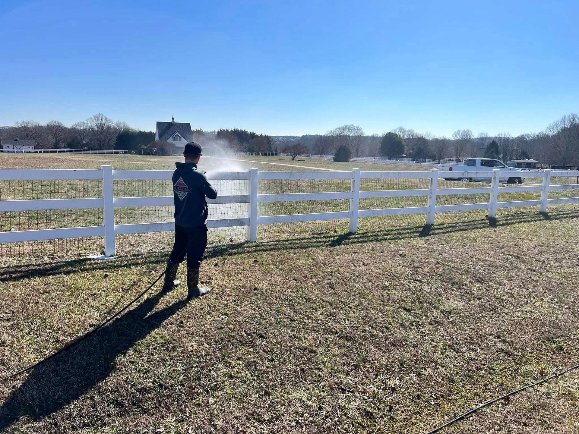 Person spraying a white fence in a field on a sunny day.
