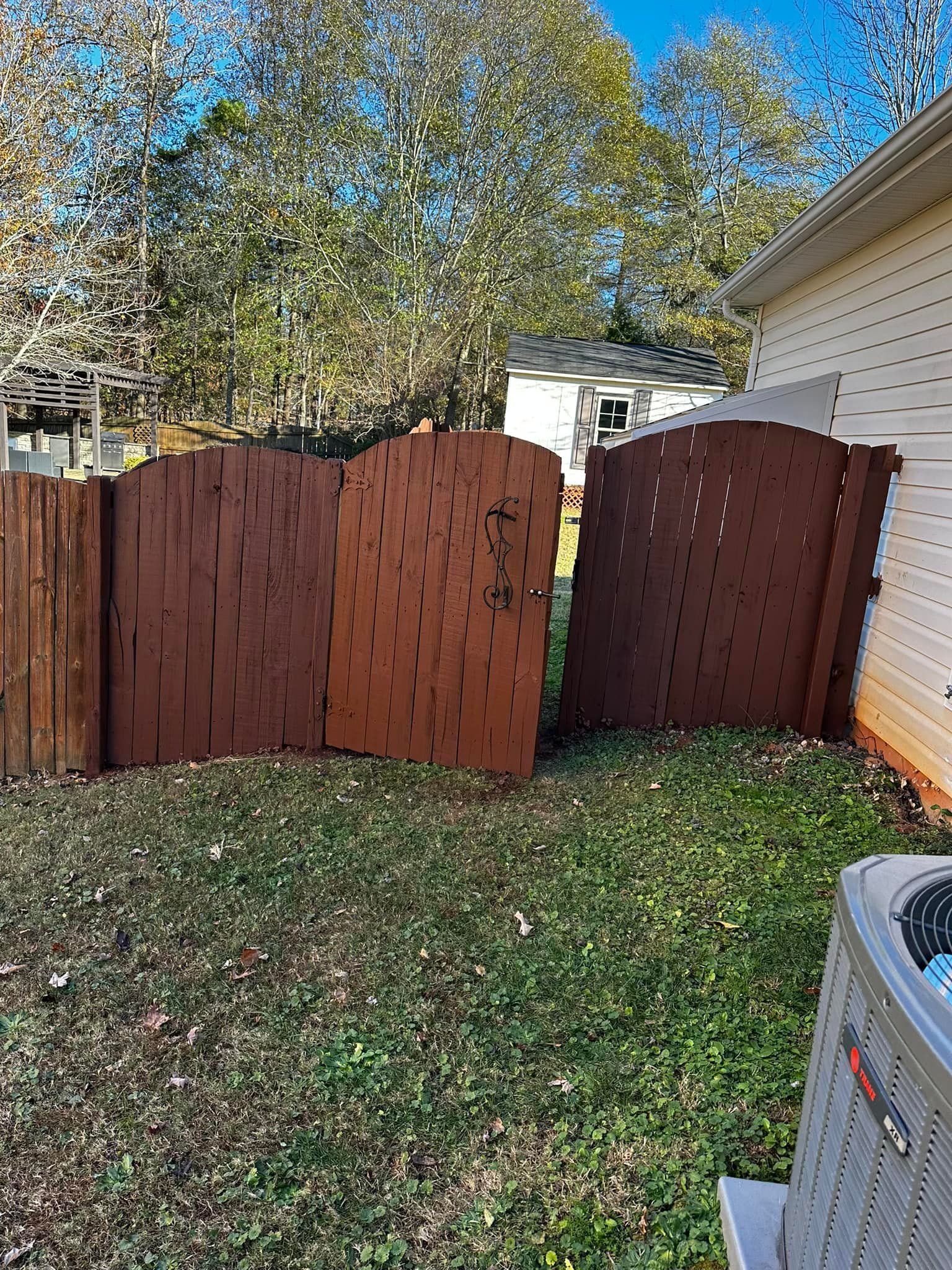 Broken brown wooden fence panels leaning against a white house and grass.