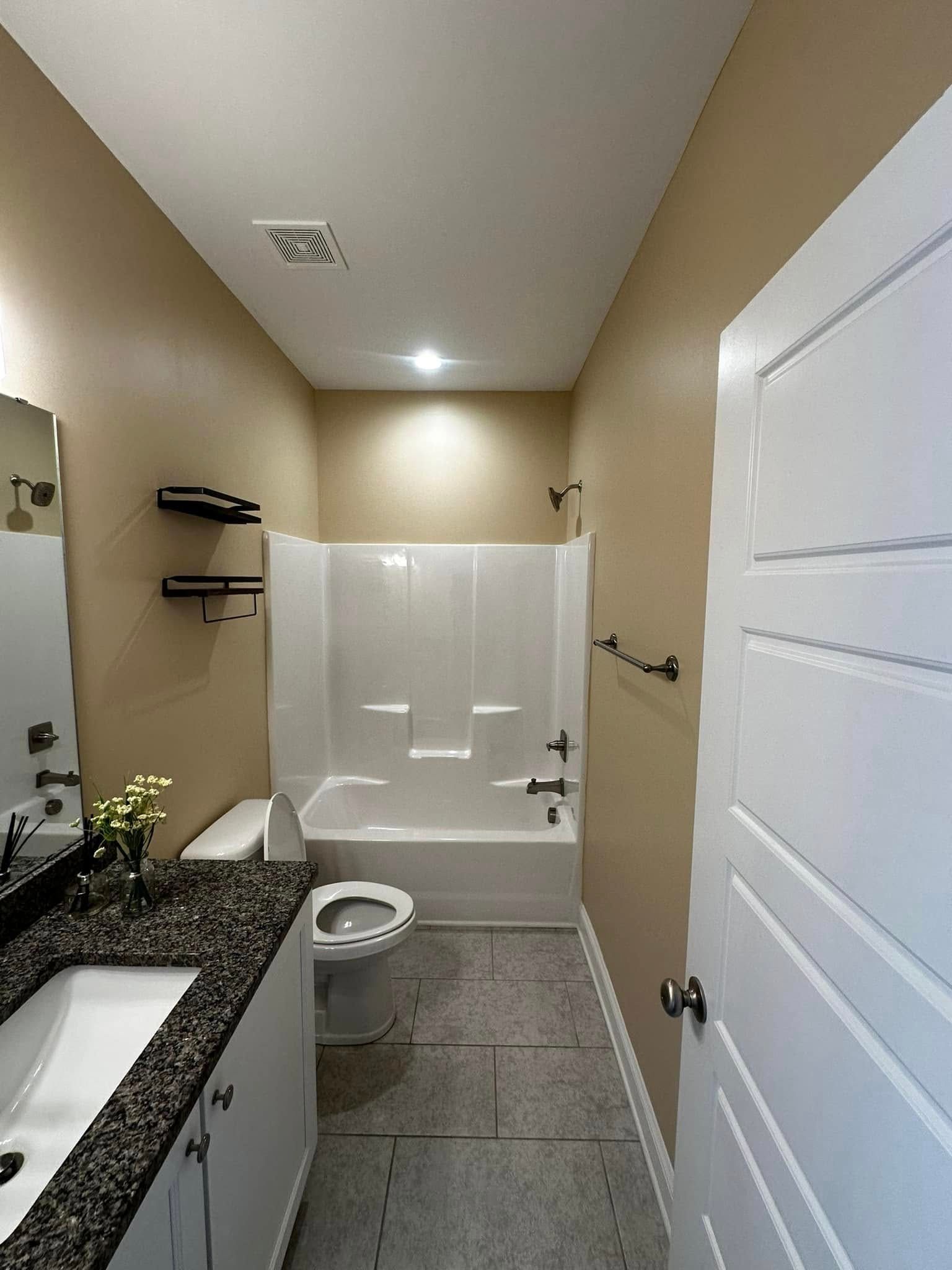Bathroom with white fixtures, beige walls, gray floor, and a closed white door.