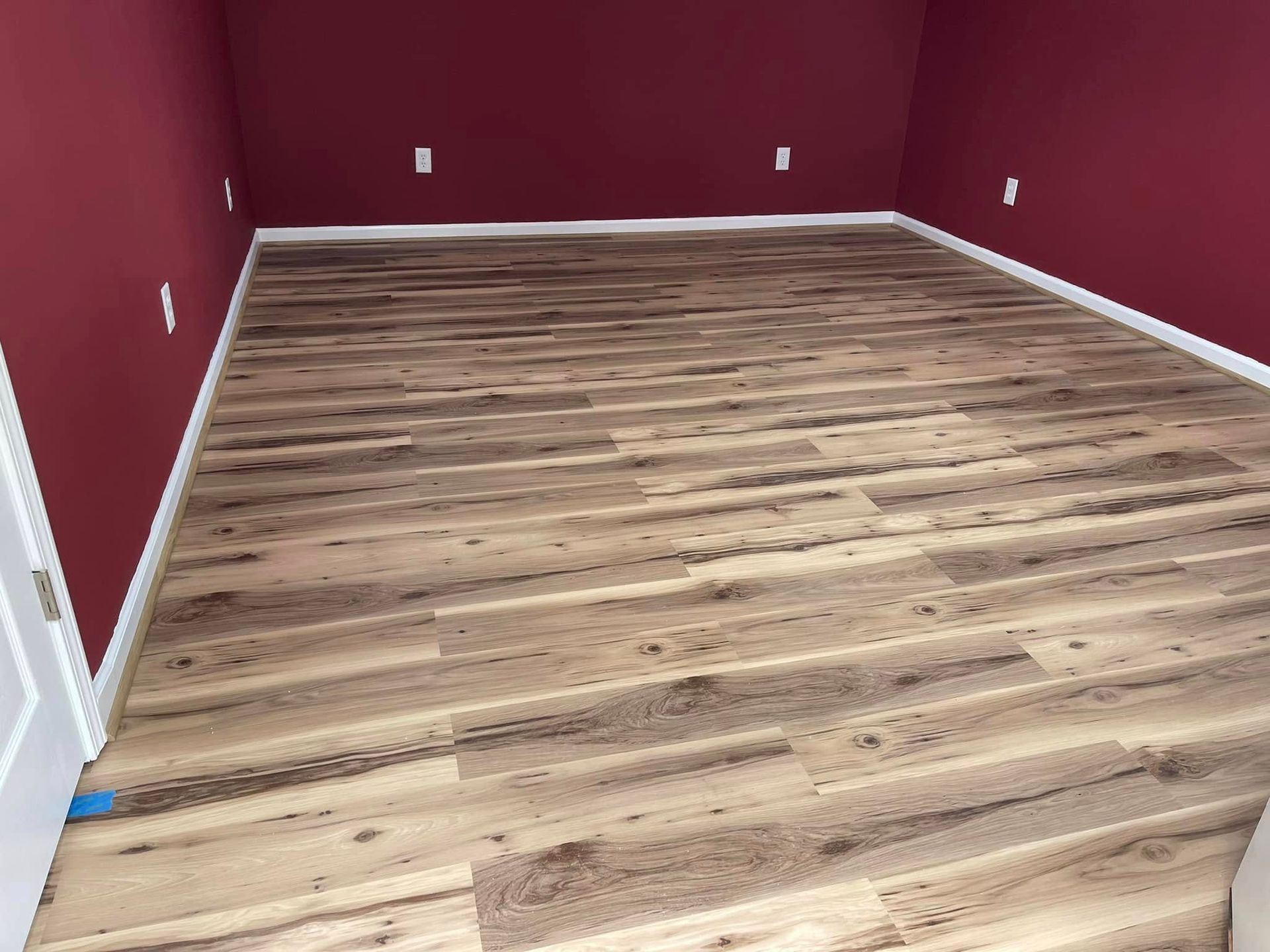 Room with red walls and wood-look flooring. White baseboards and outlets are visible.