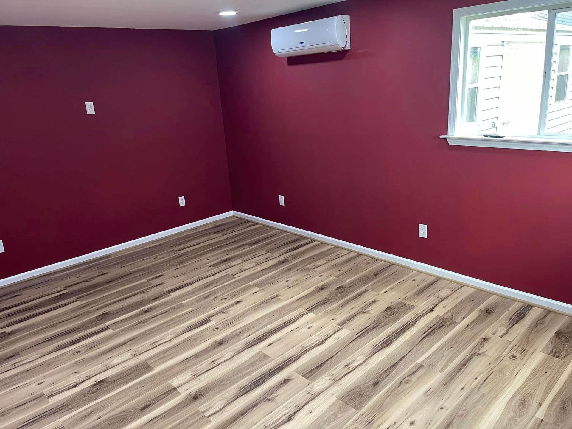 Room with burgundy walls, wood-look flooring, white trim, and a window. A/C unit is mounted on the wall.