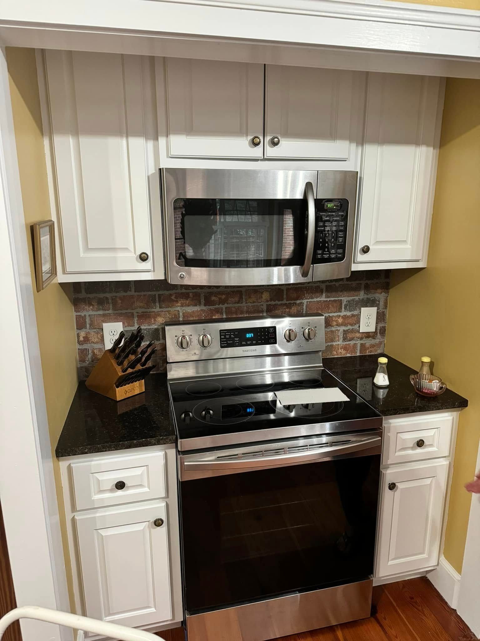 Kitchen with white cabinets, stainless steel appliances, brick backsplash, and black countertops.