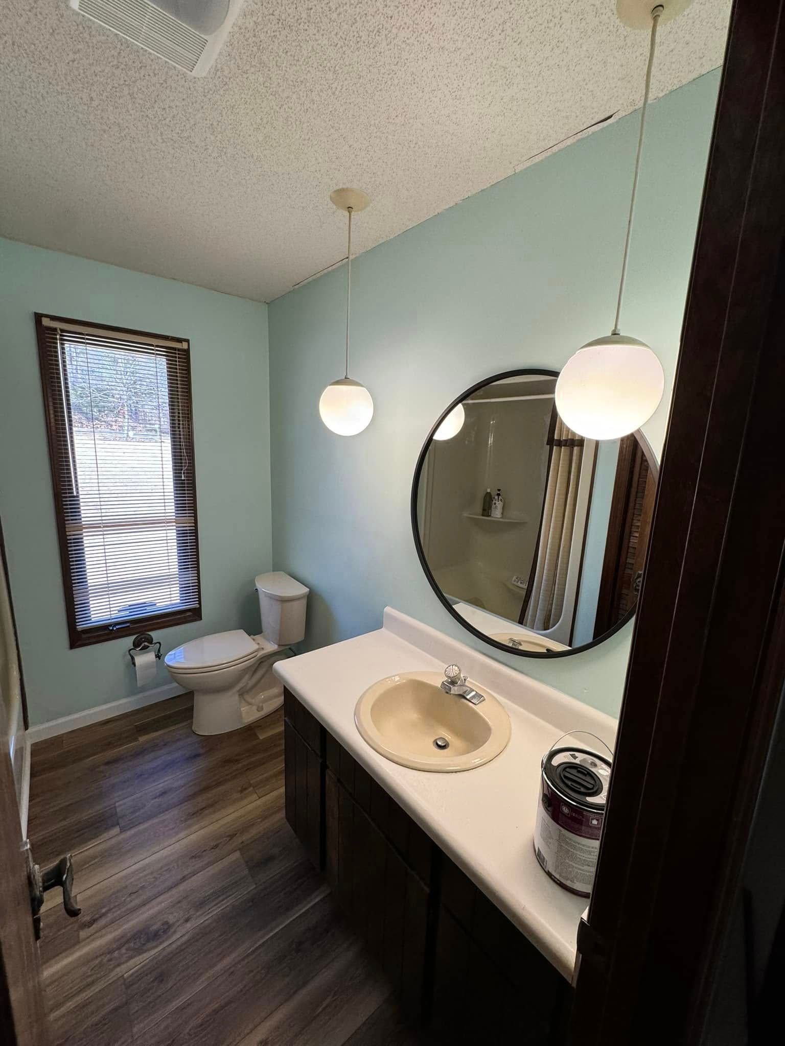 Bathroom with pale blue walls, dark vanity, round mirror, and two globe pendant lights.