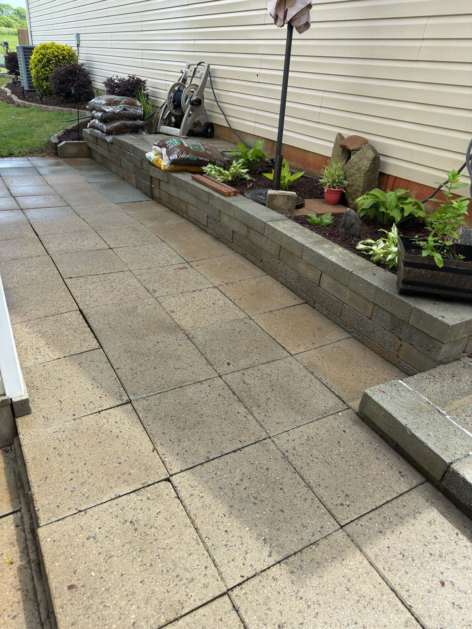 Patio with gray concrete pavers, retaining wall with plants, and a house exterior.