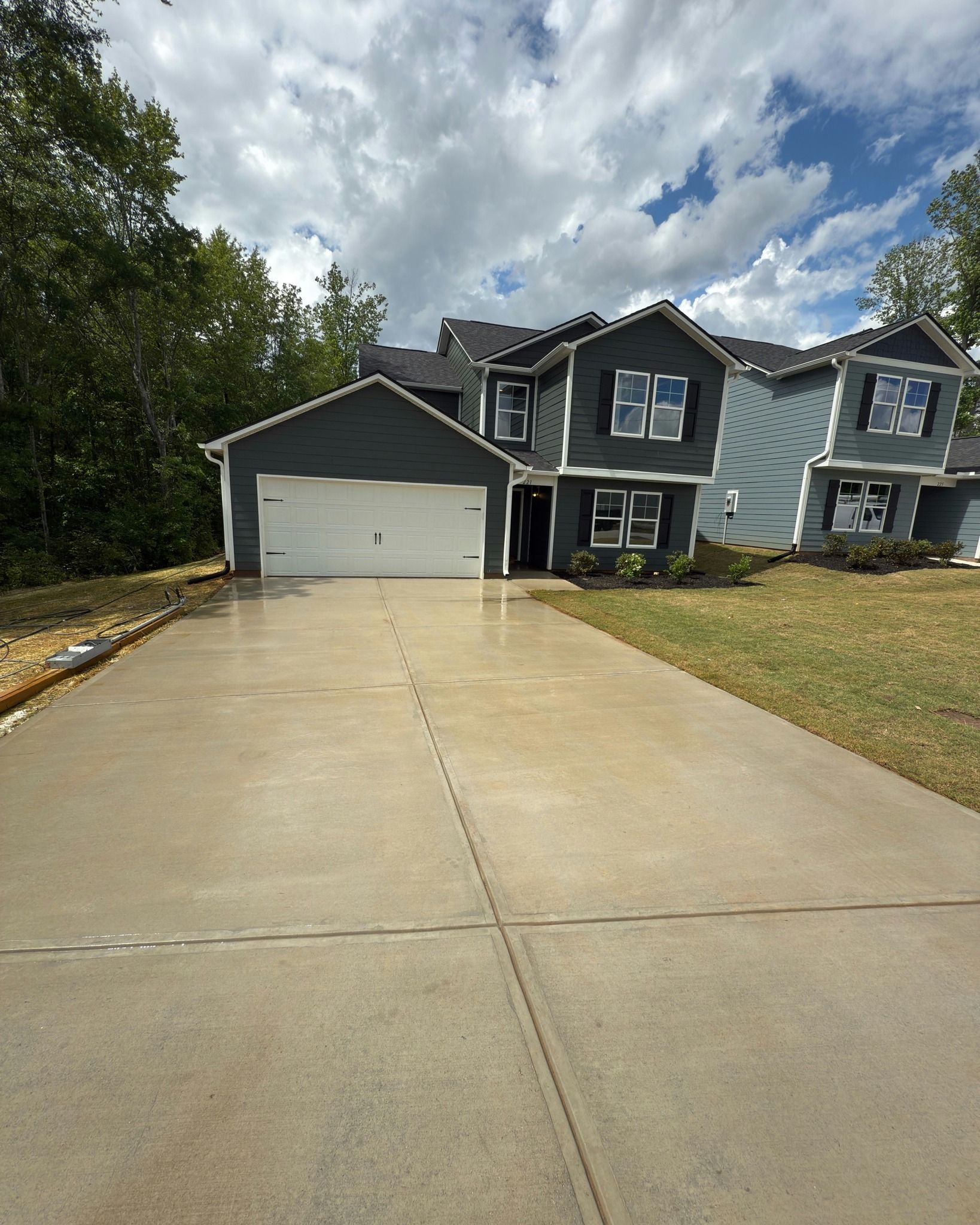 Two-story house with gray siding, white garage door, long driveway, and blue sky.