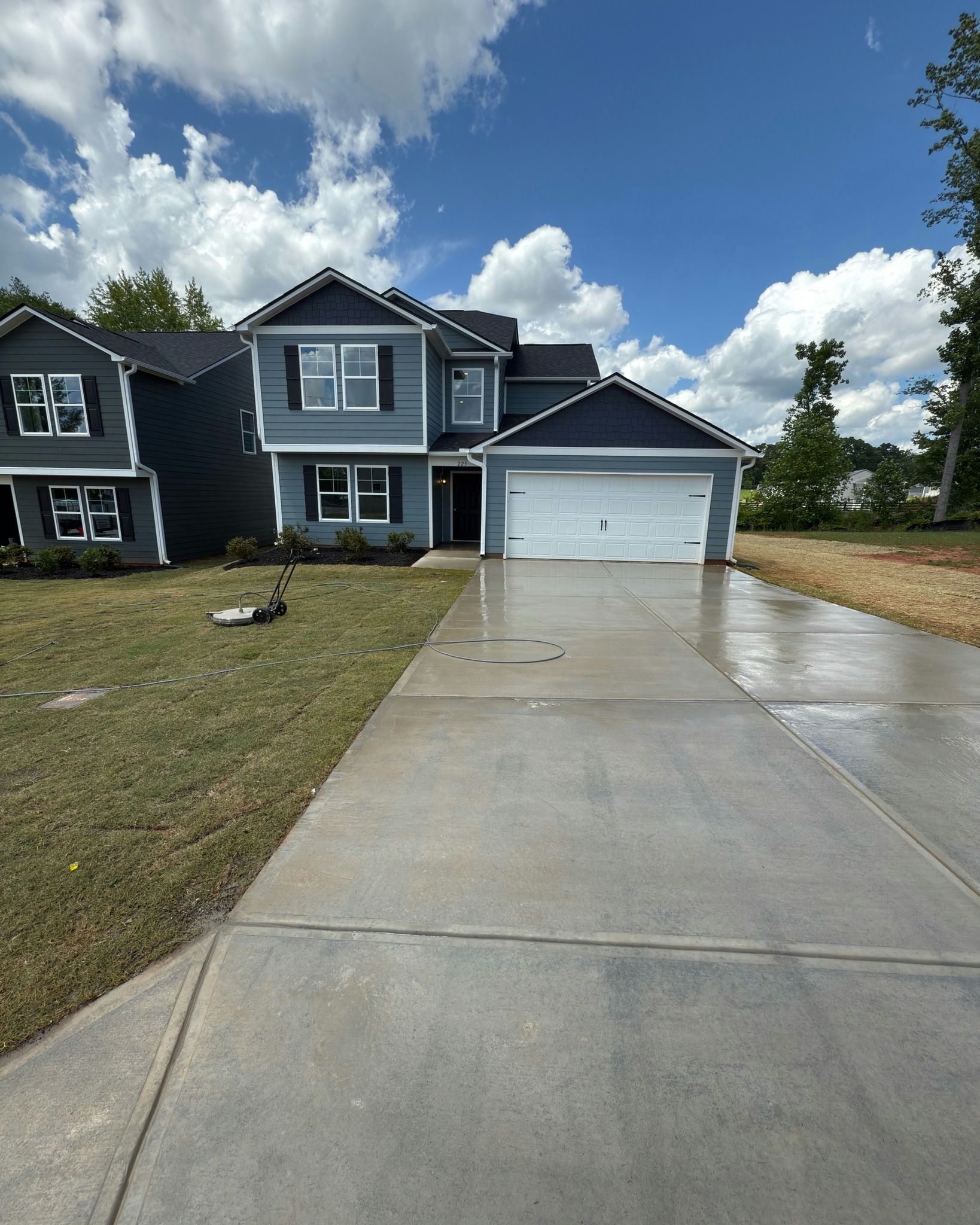 Two-story blue house with white garage door, wet driveway, and blue sky.