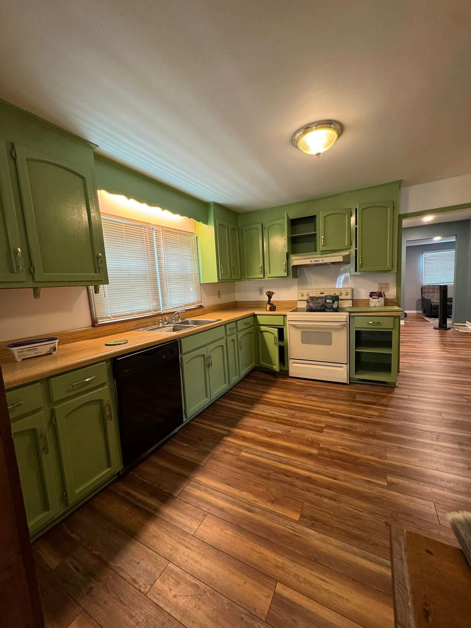 Green kitchen cabinets, black appliances, and wooden floors.
