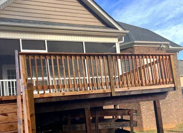 Wooden deck attached to a house with a screened porch and blue sky.