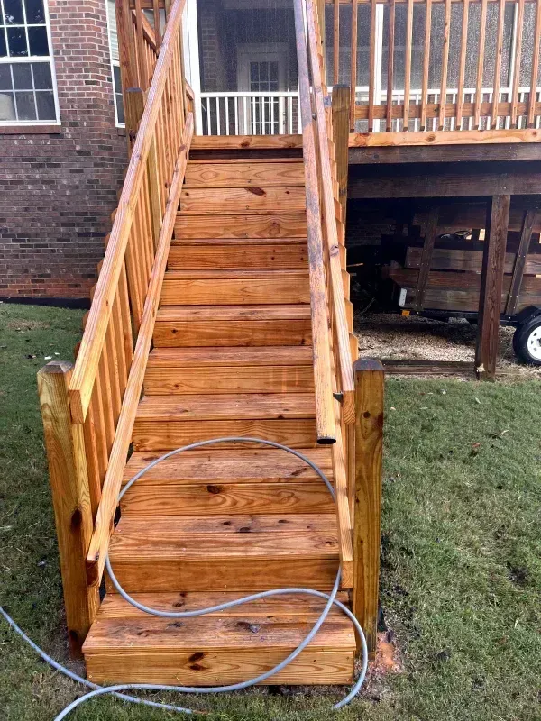 Wooden outdoor staircase leading up to a deck, with handrails, set in grassy yard.