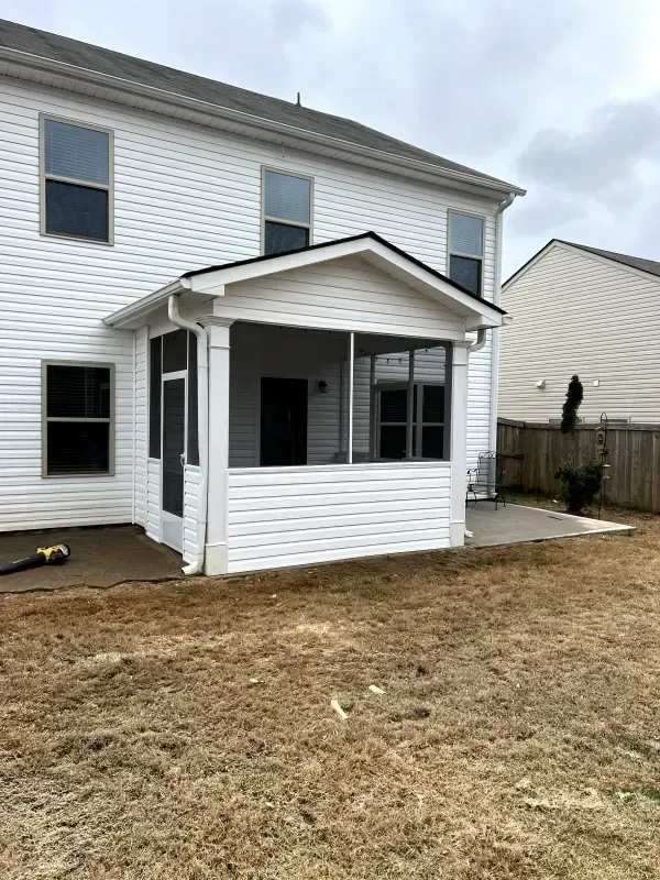 White house with a screened-in porch, concrete patio, and fenced backyard. Brown grass in foreground.