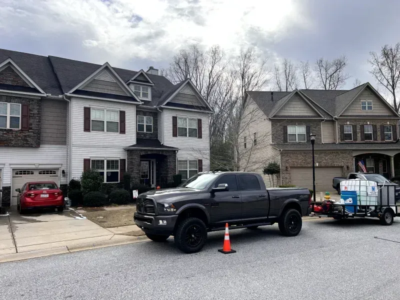 A dark gray pickup truck with trailer parked in front of two-story houses on a cloudy day.