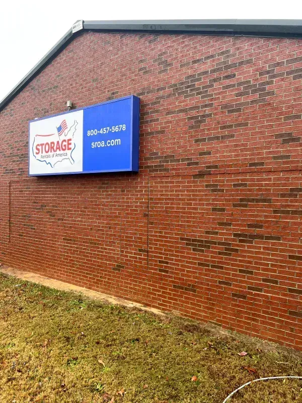 Storage facility sign on a brick building with phone number and website address.