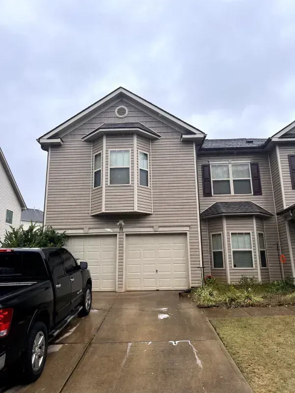 Two-story townhouse with beige siding, two-car garage, and black pickup truck parked in driveway.