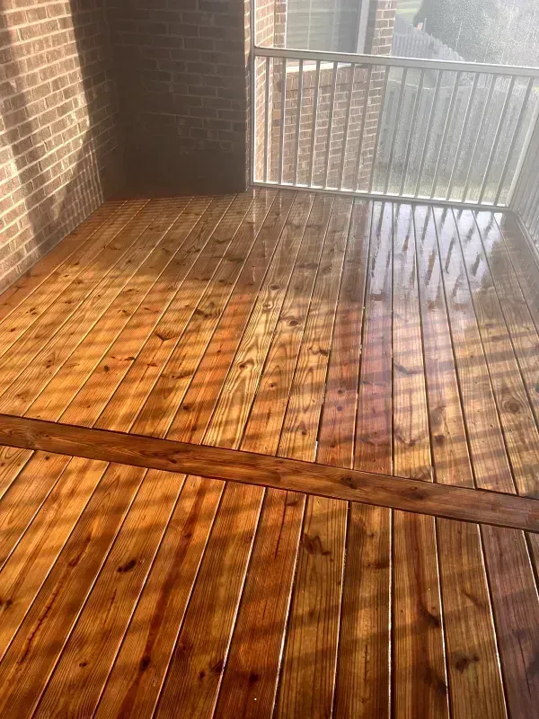 Newly stained wooden deck with a brick wall and a white railing.