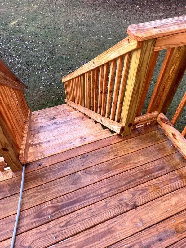Wooden deck and stairs with railing, stained brown, leading down to green grass.