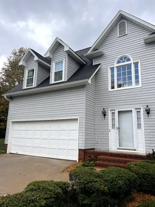 Two-story gray house with white garage door and entrance, brick steps, and bushes.