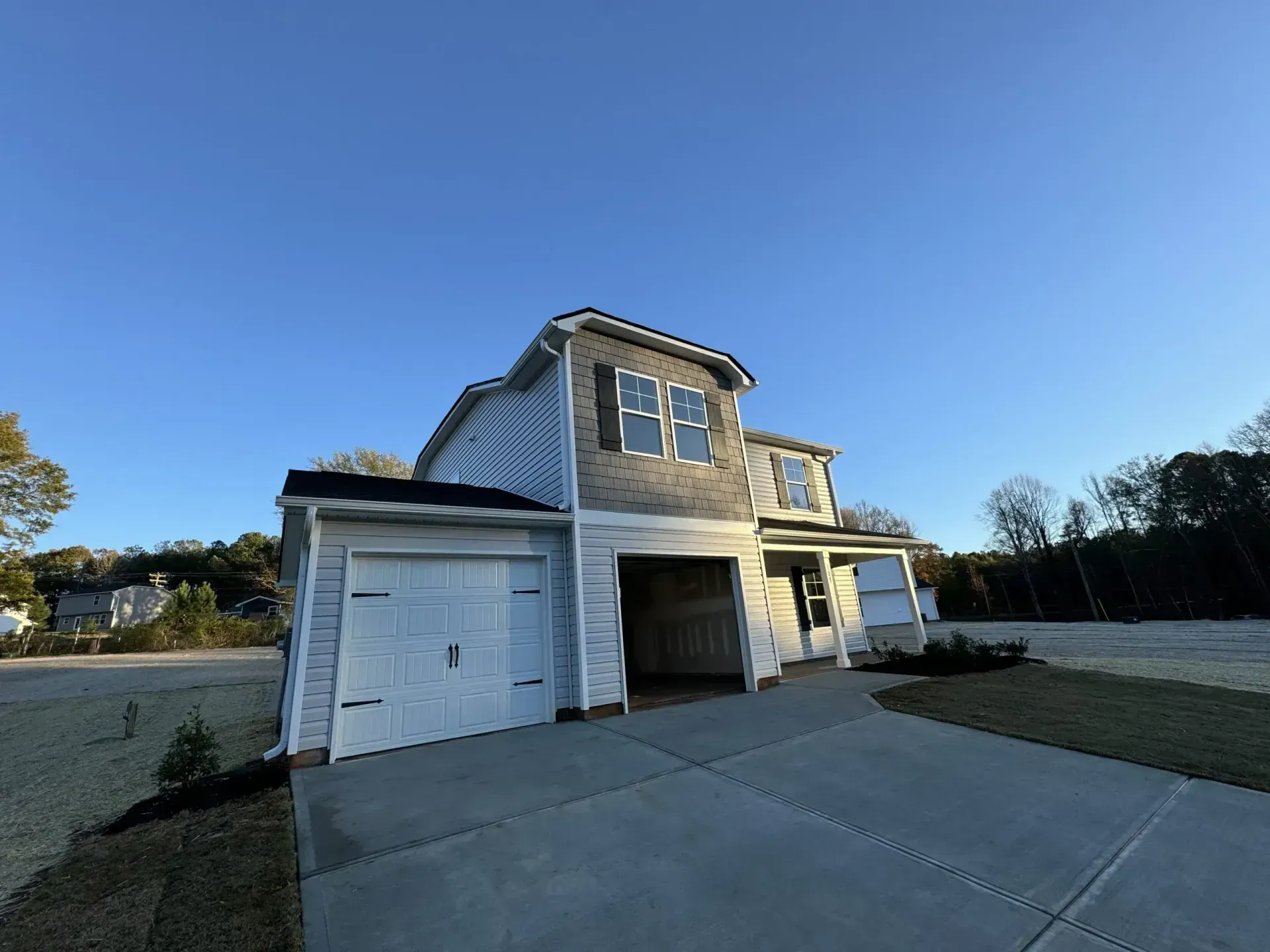 Two-story house with a two-car garage, gray siding, and a driveway on a sunny day.