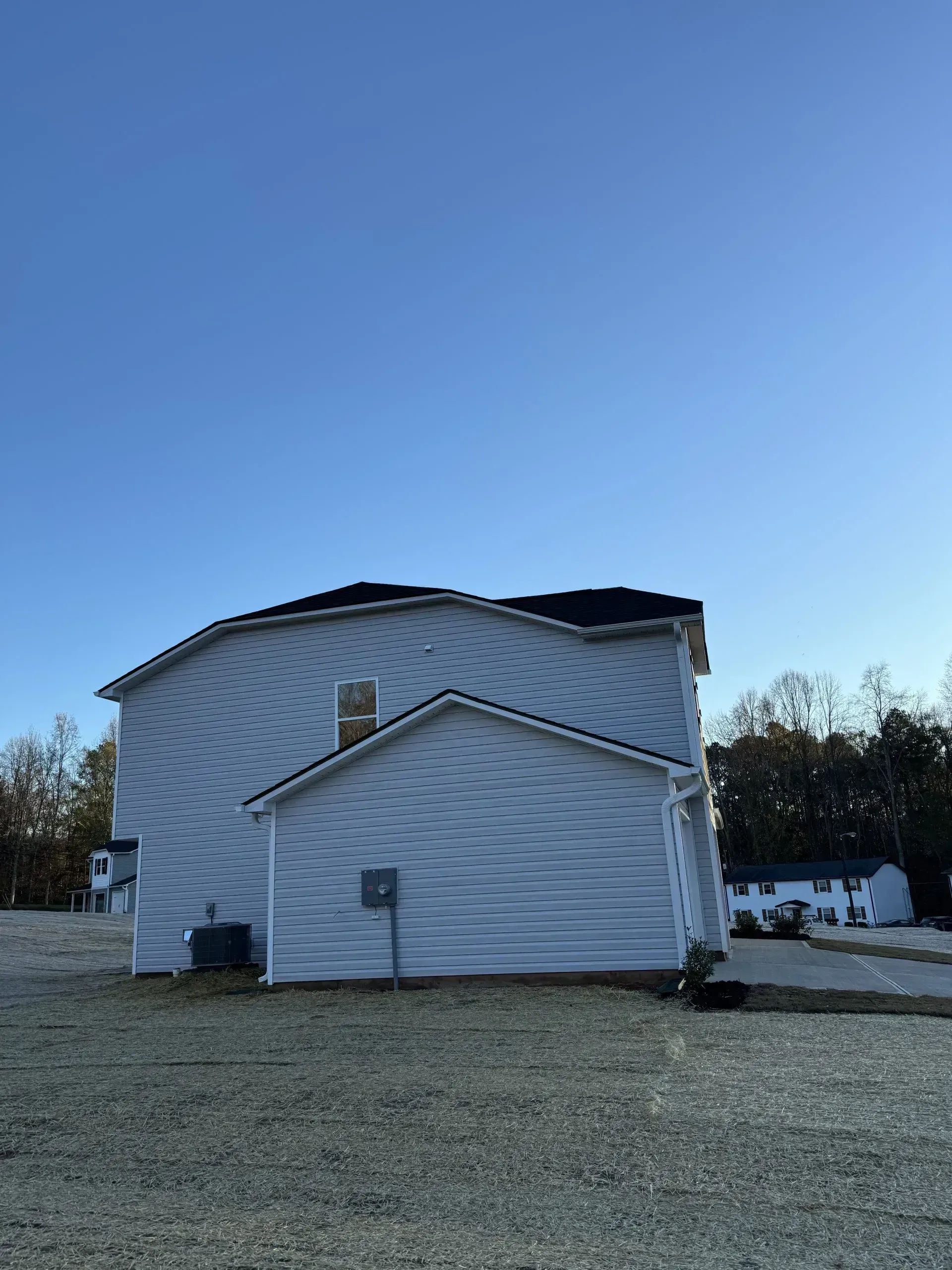 Two-story light blue house with a dark roof on a clear day; gravel in the foreground.