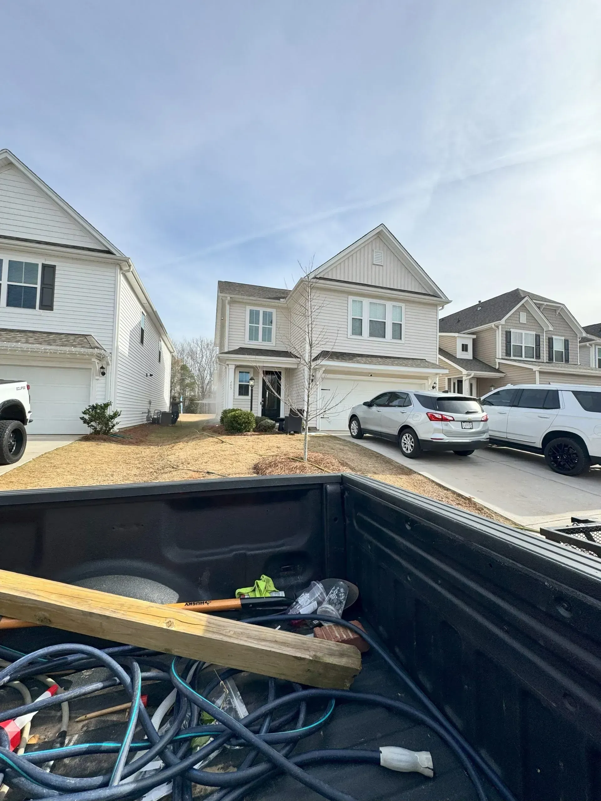 Two-story house with a car in front. The foreground shows the bed of a truck with tools.