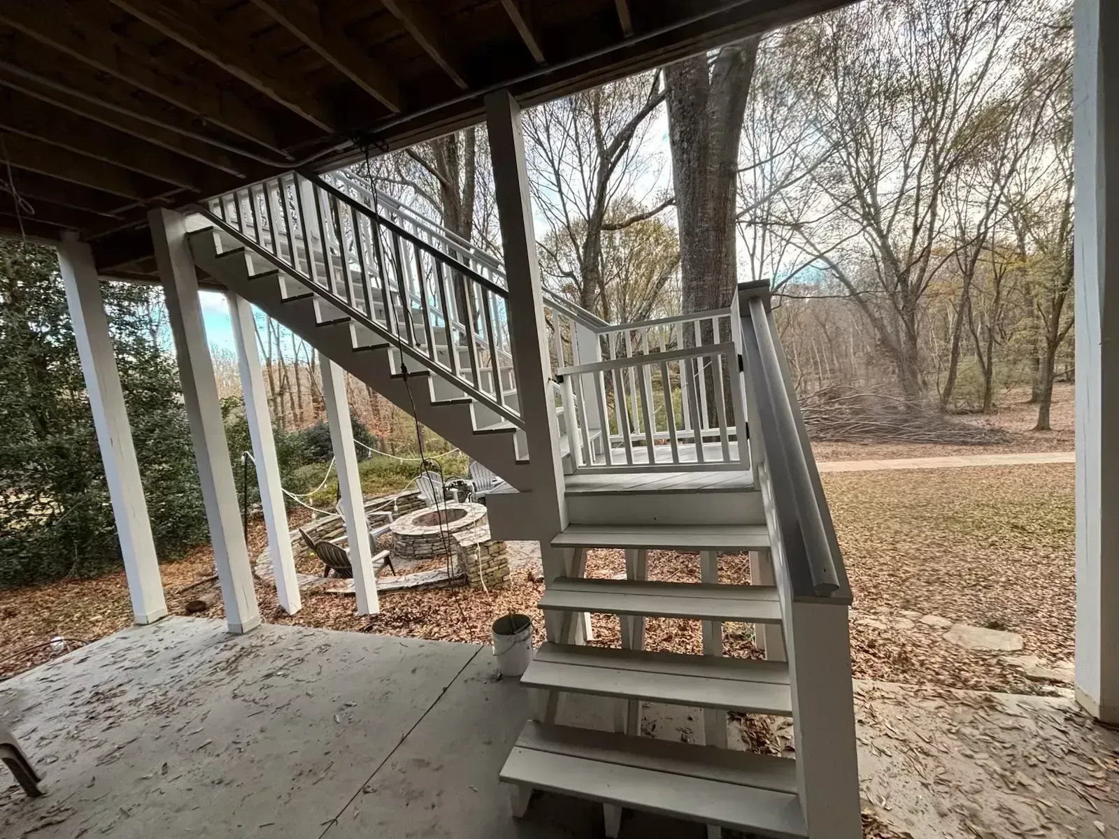 White staircase leading up from a covered patio to a wooded yard.
