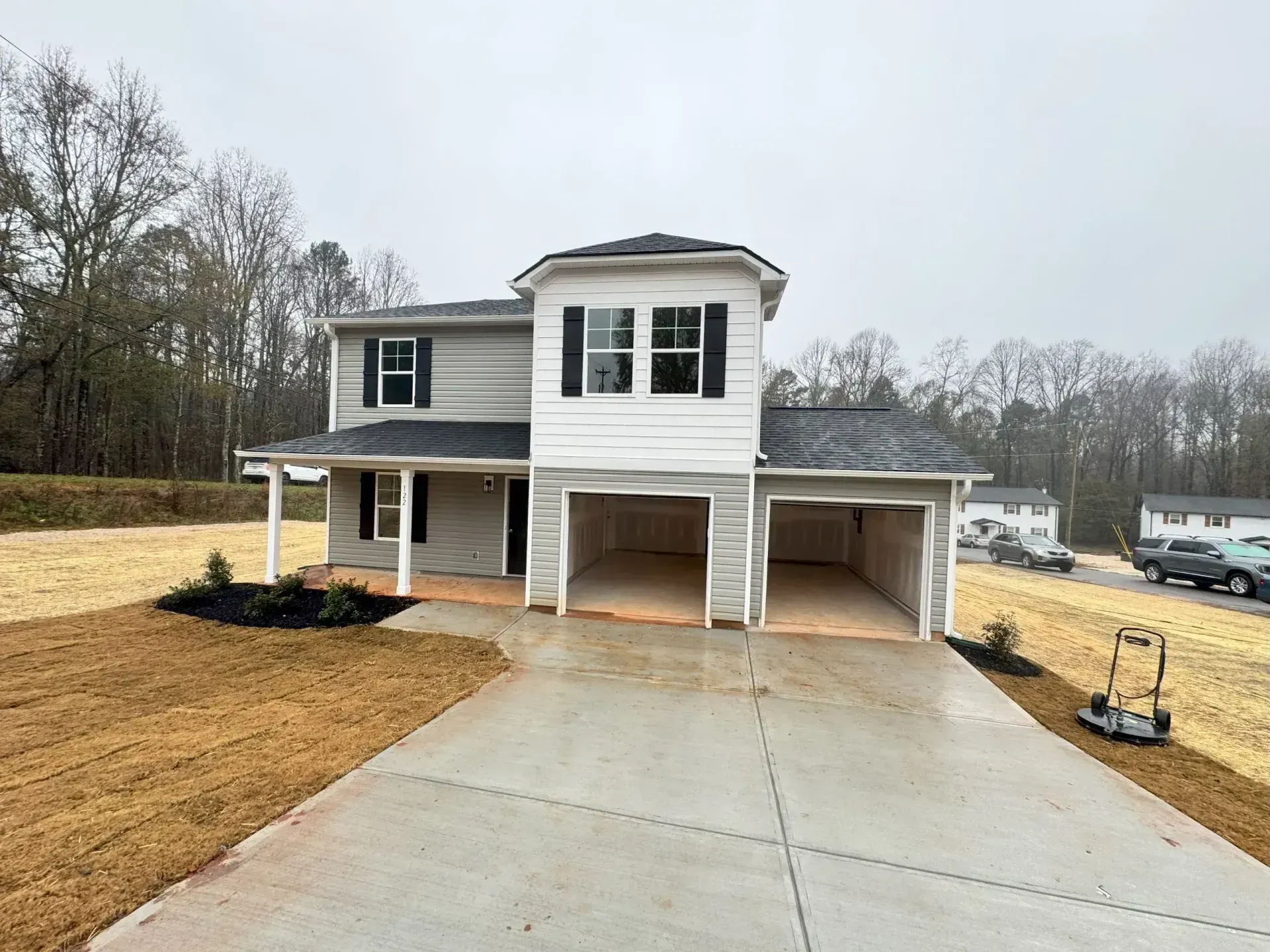 Two-story house with two open garage bays. Gray siding, black shutters, and overcast sky.