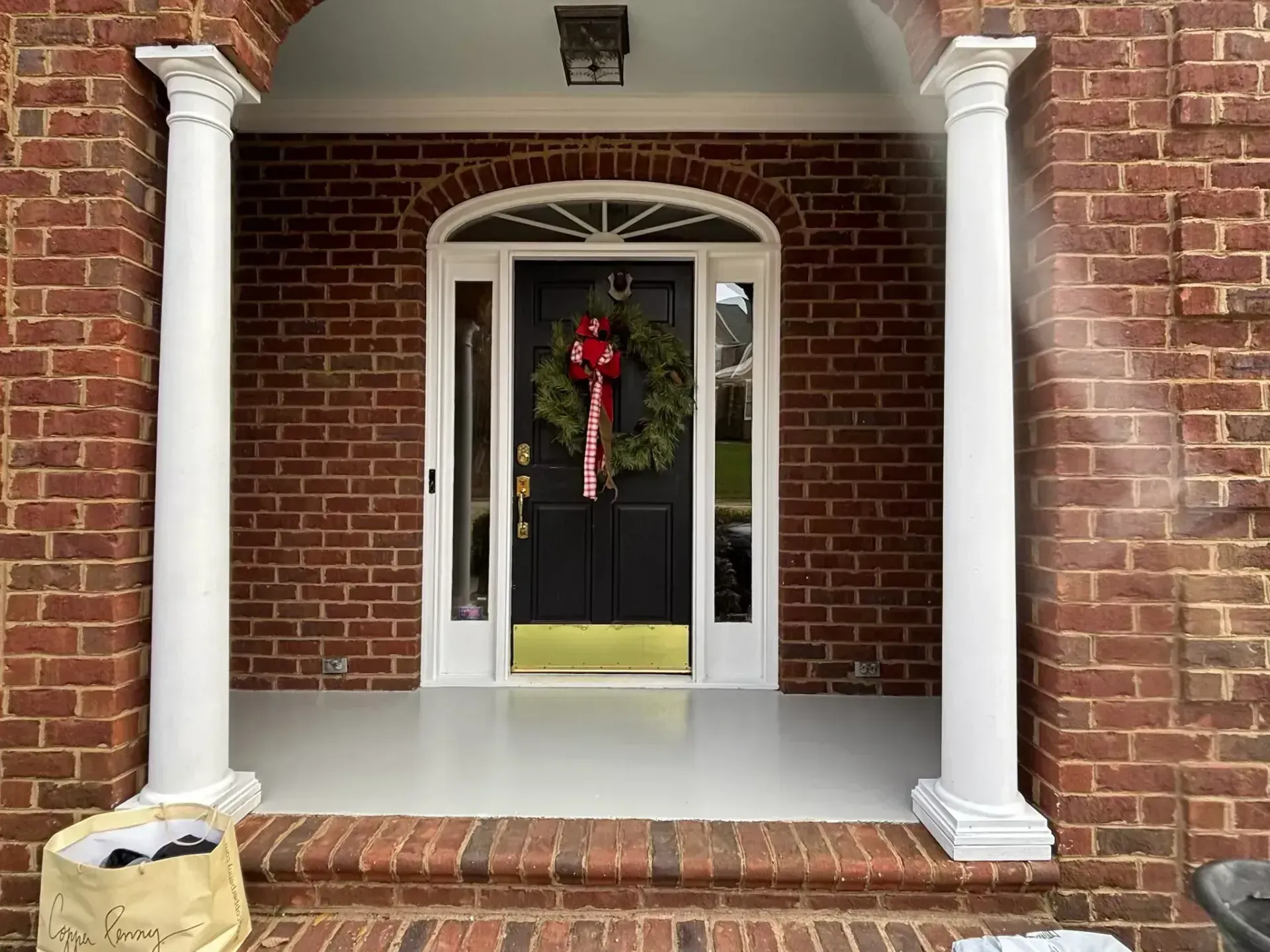 Brick porch with white pillars frames a black door with a Christmas wreath.