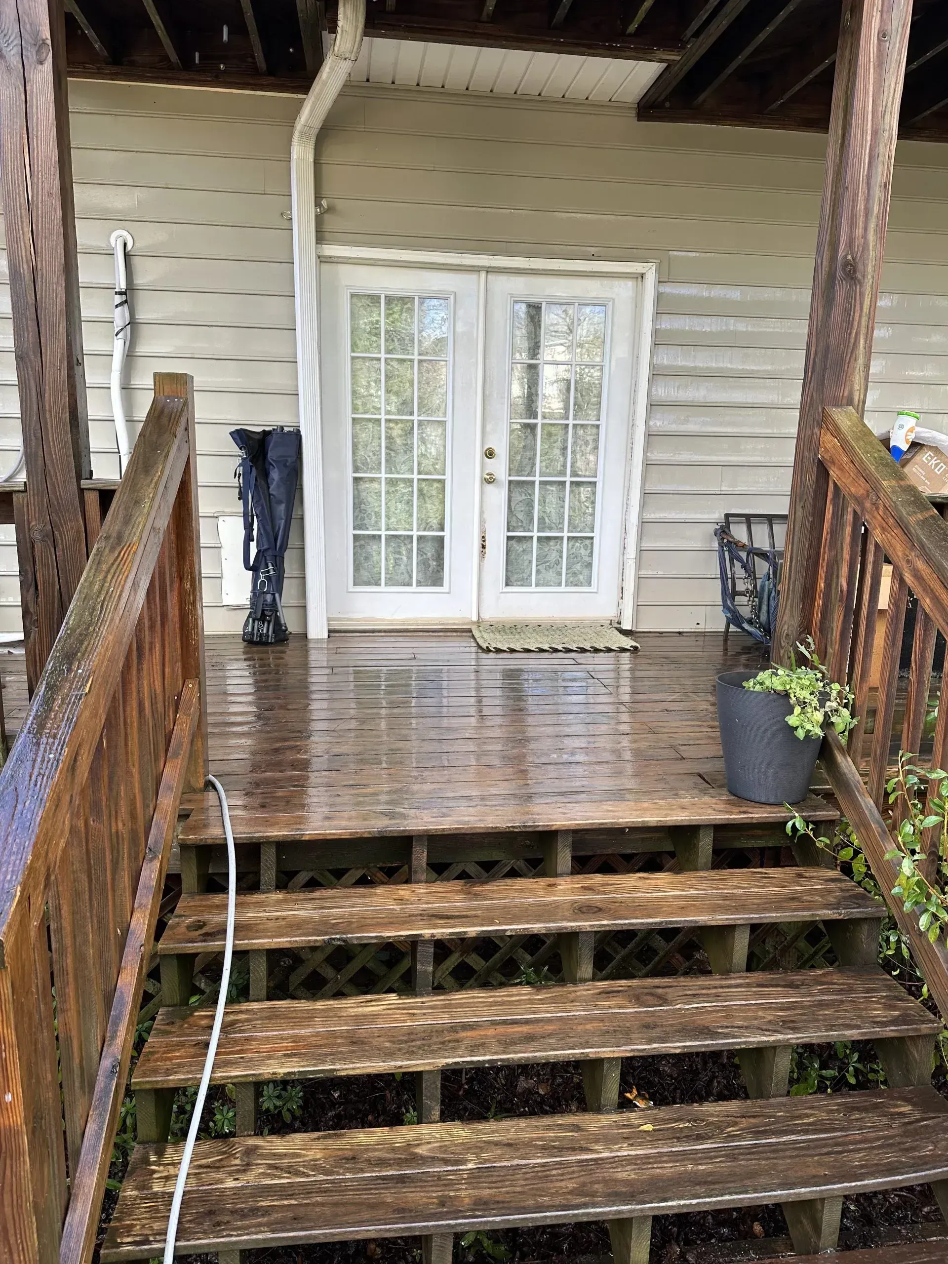 Wooden staircase leading up to white French doors on a porch with wet decking.
