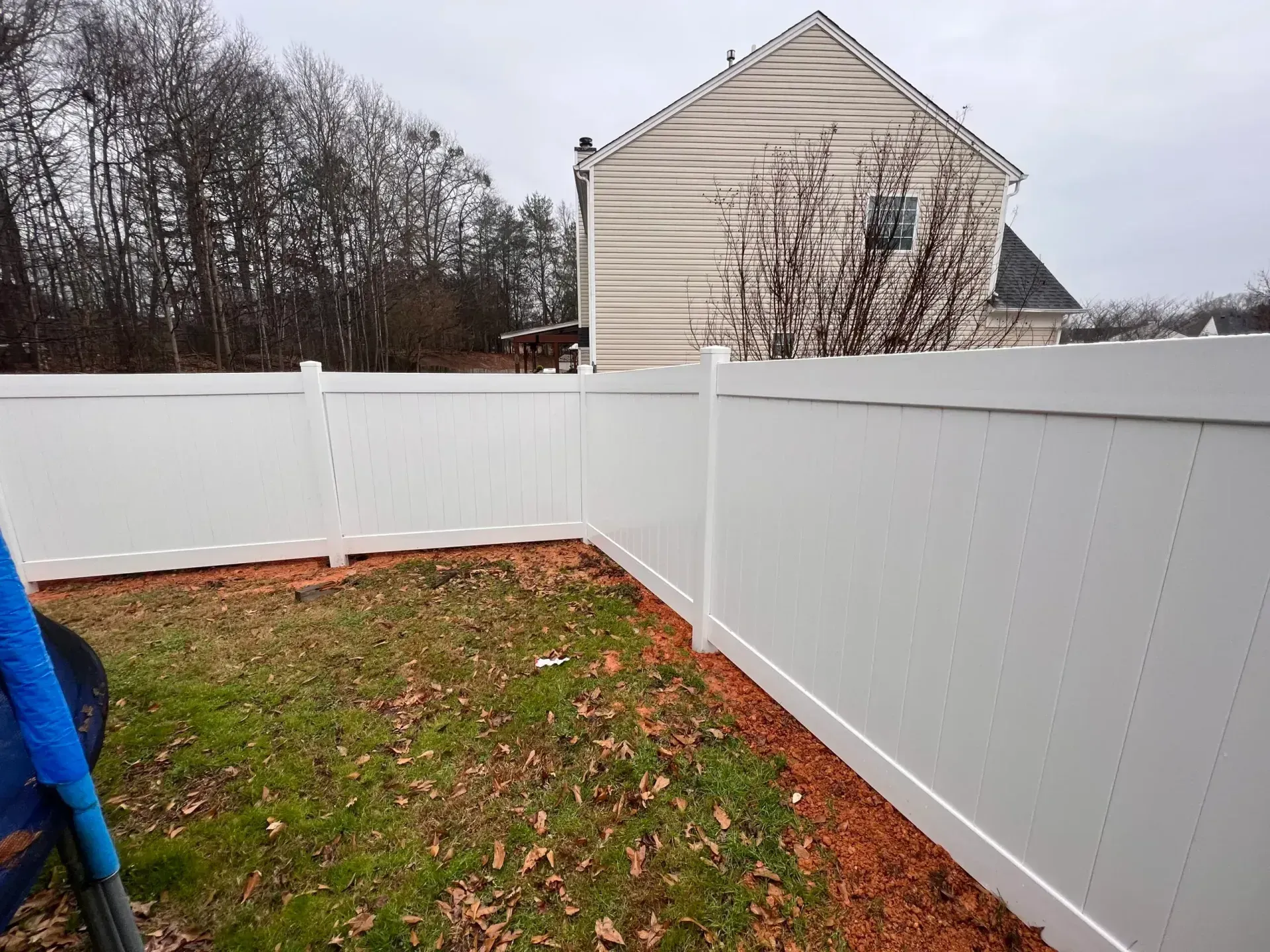 White vinyl fence surrounding a grassy backyard with a house in the background. Overcast sky.