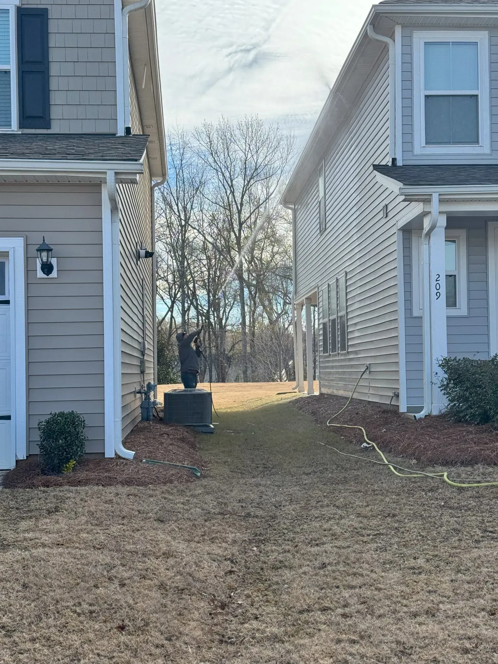 Two-story houses with a narrow grassy space between them; trees in the background.