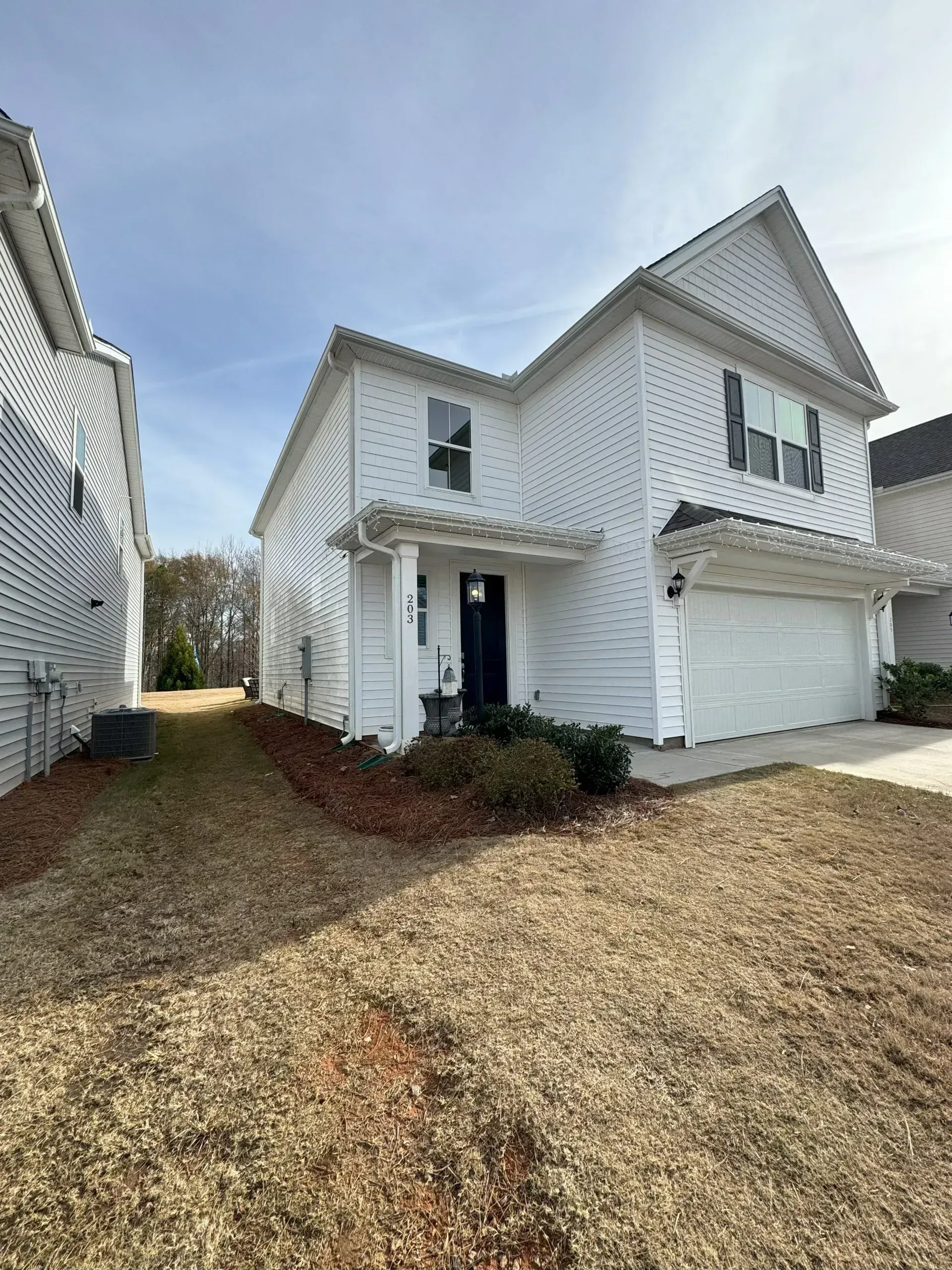 White two-story house with a small porch, garage, and brown lawn.