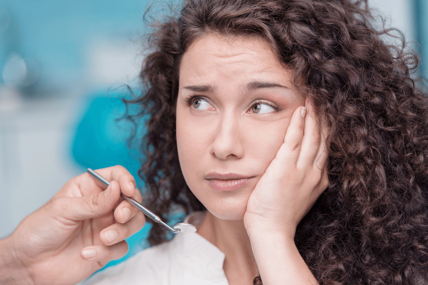 Una mujer en una clínica se toca la mejilla mientras un instrumento dental se acerca a su boca.