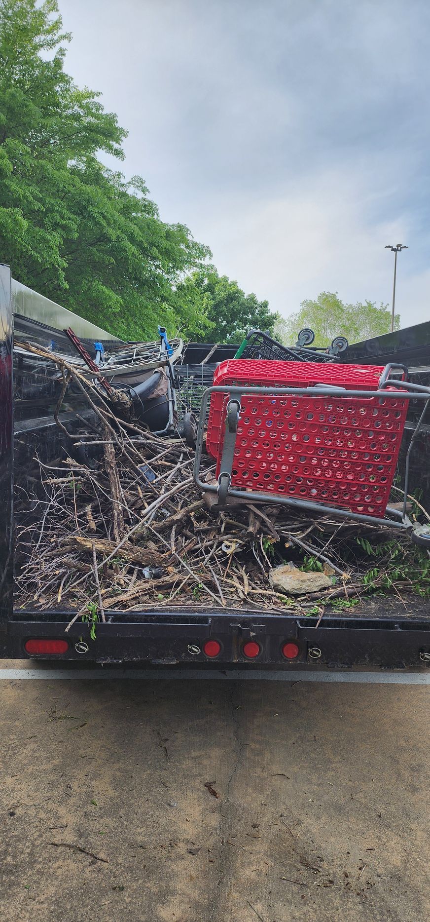 A red shopping cart is sitting in the back of a dumpster.