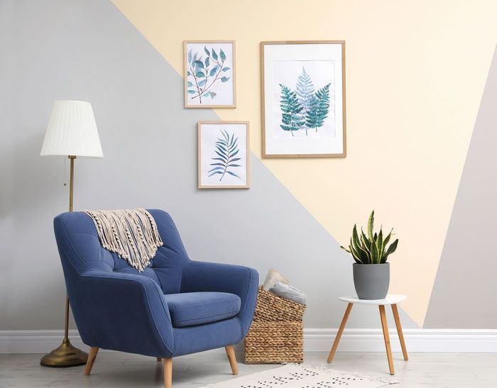 A living room with a blue chair , lamp , table and paintings on the wall.