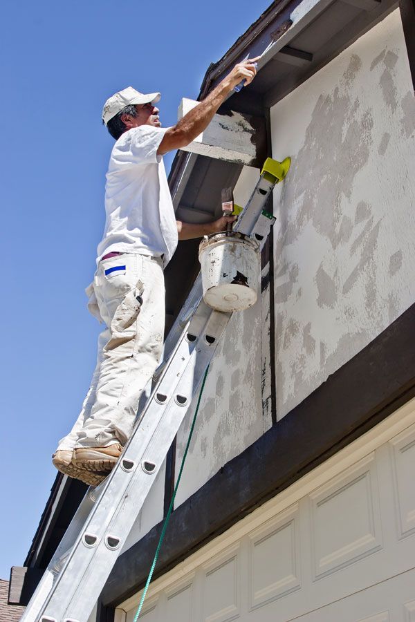 A man is standing on a ladder painting a building.