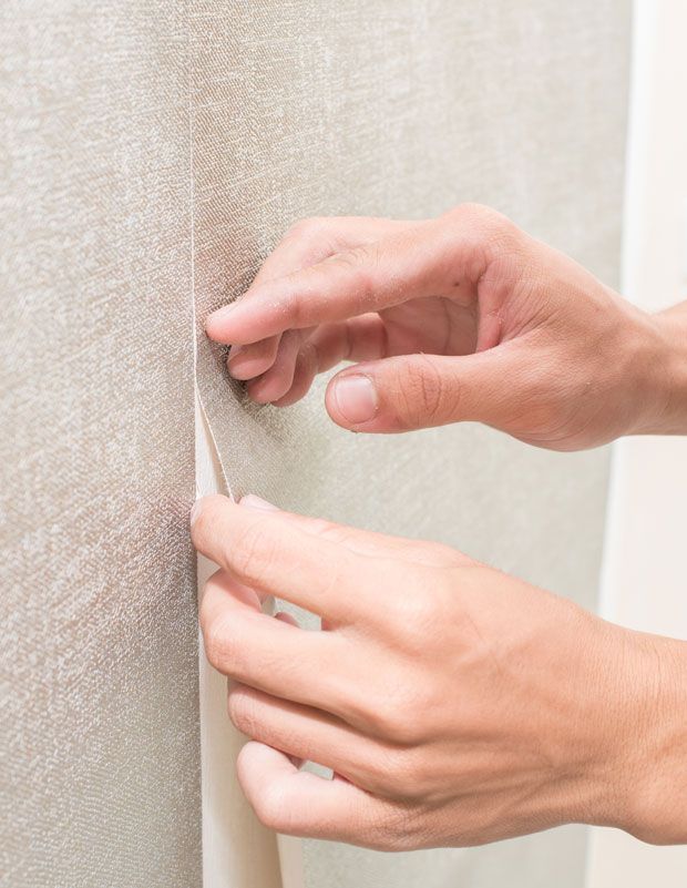 A person is peeling off a piece of wallpaper from a wall.