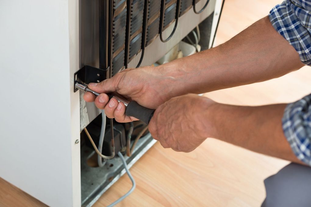 A man is fixing a refrigerator with a screwdriver.