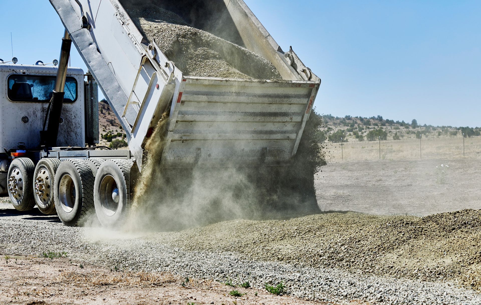 A truck dumps gravel at a busy construction site in bright sunlight. A truck dumps gravel at a busy construction site in bright sunlight.