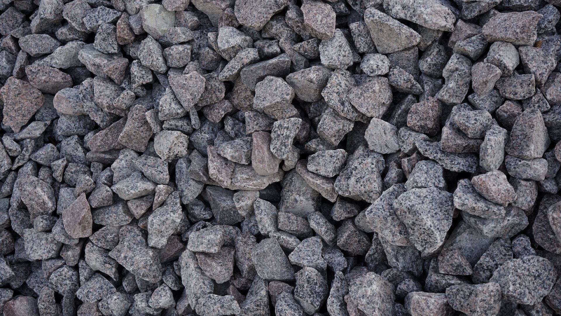 Grey crushed stone mounds with sharp, angular textures in close view.. Grey crushed stone mounds with sharp, angular textures in close view..