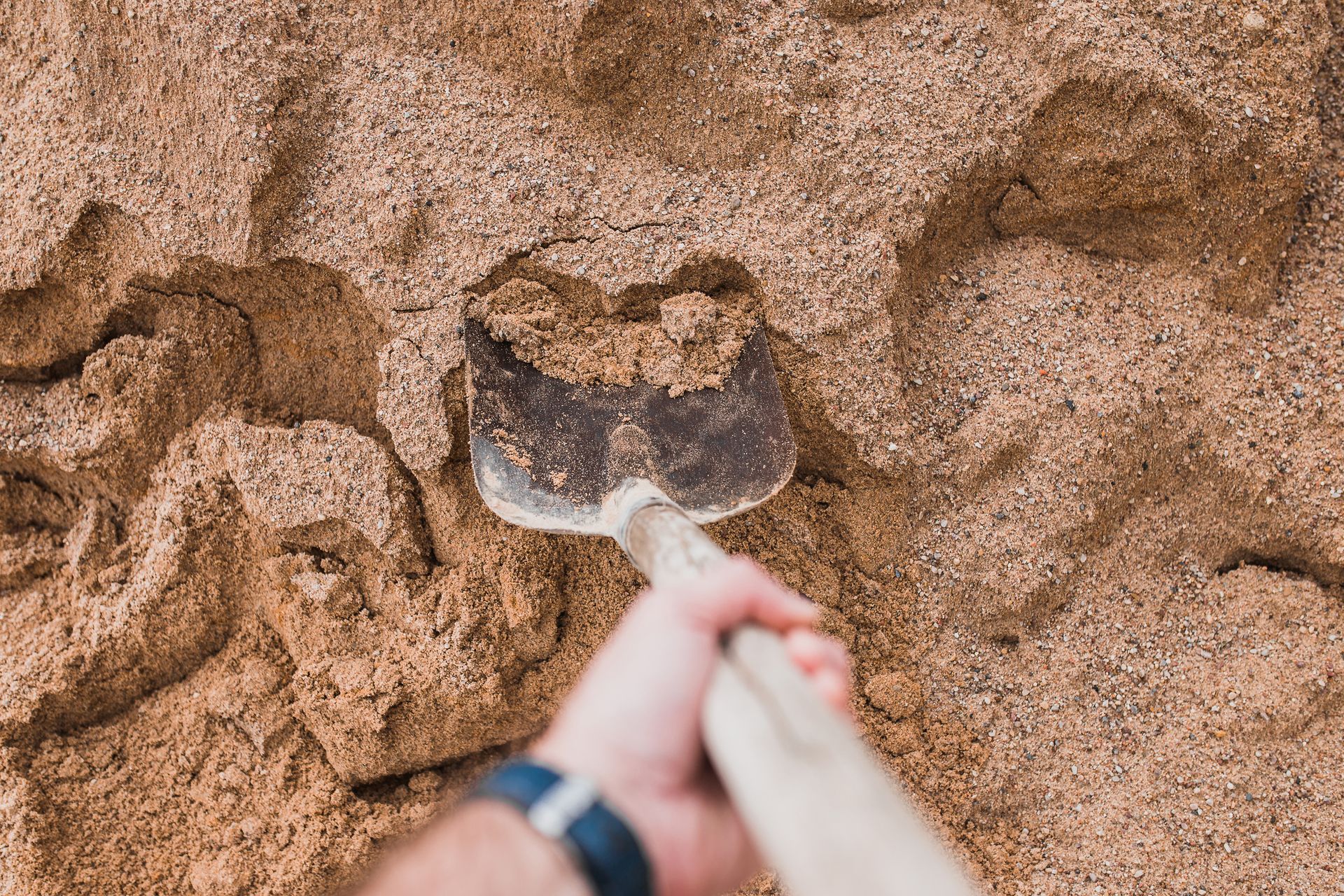 A person is digging in the sand with a shovel.