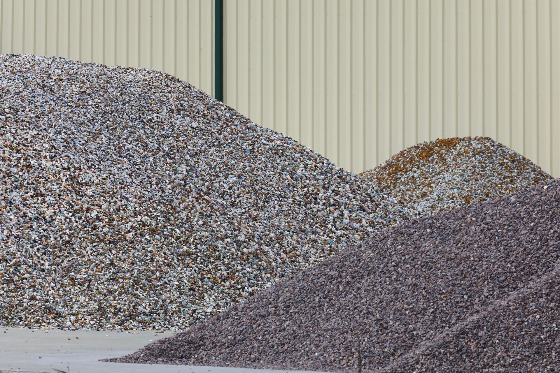 Large gravel piles stacked in an outdoor supply yard beside a corrugated metal wall.
