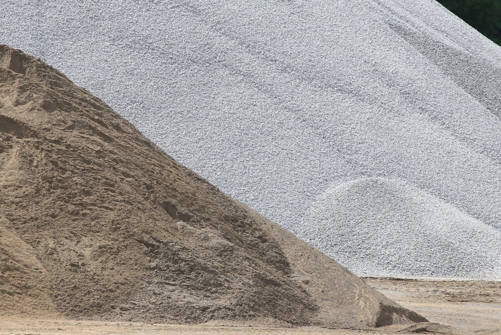 Large piles of brown sand and gray gravel at construction materials yard.