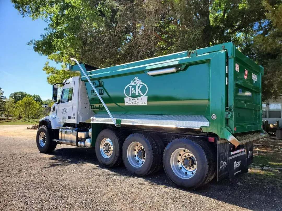 A truck from J & K Materials & Trucking is below a tree, at daylight.