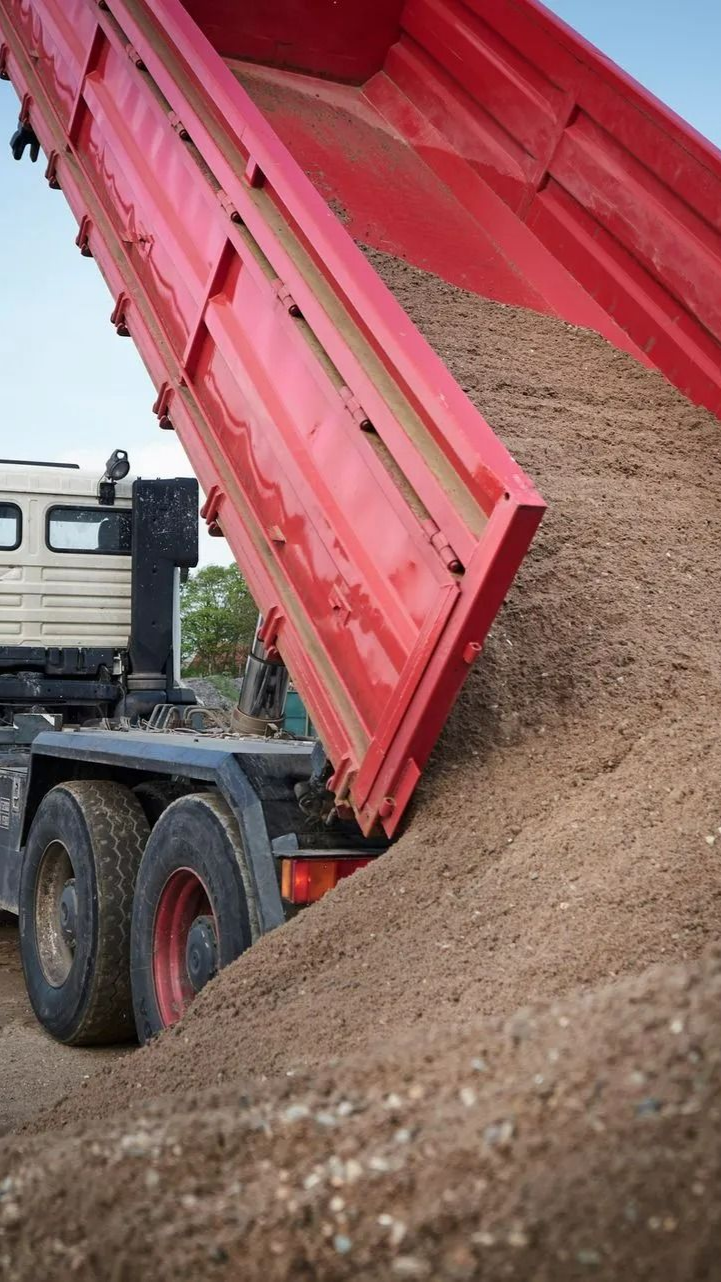 A construction truck dumps a pile of fine earth on the ground.
