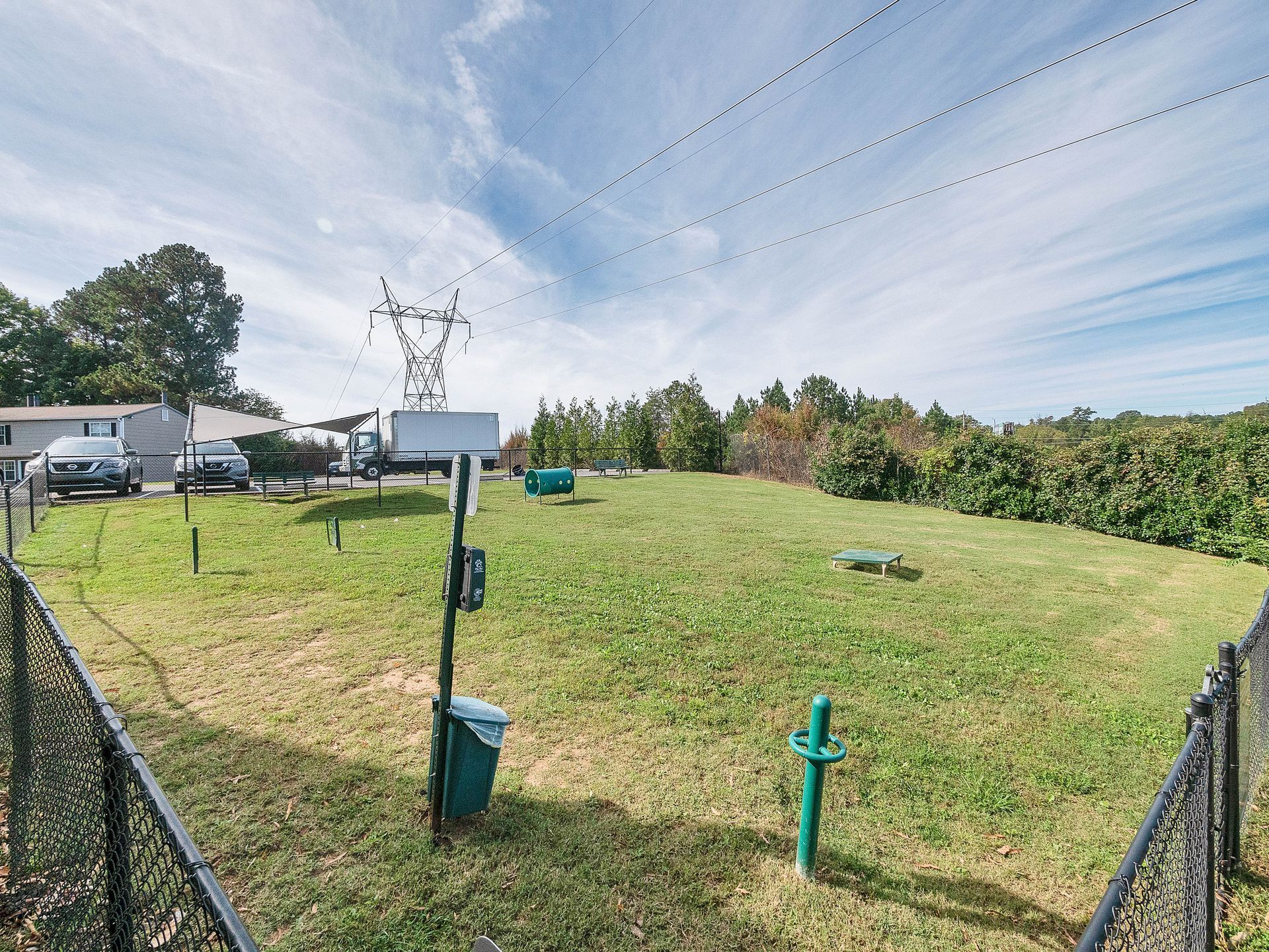 A grassy, fenced lot under a blue sky, featuring a tall utility pole and several pipes and ground markers.