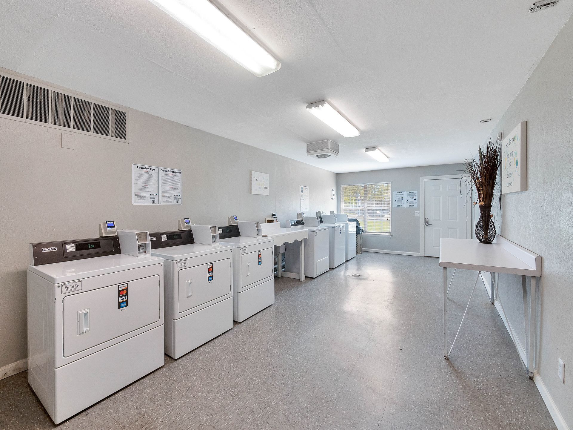 A bright, modern laundry room with white machines arranged against a wall, neutral walls, and a side folding table.