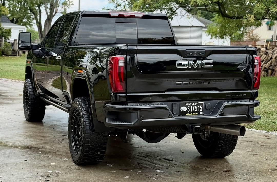 Black GMC Sierra truck parked on a wet driveway, tires visible, rear view.