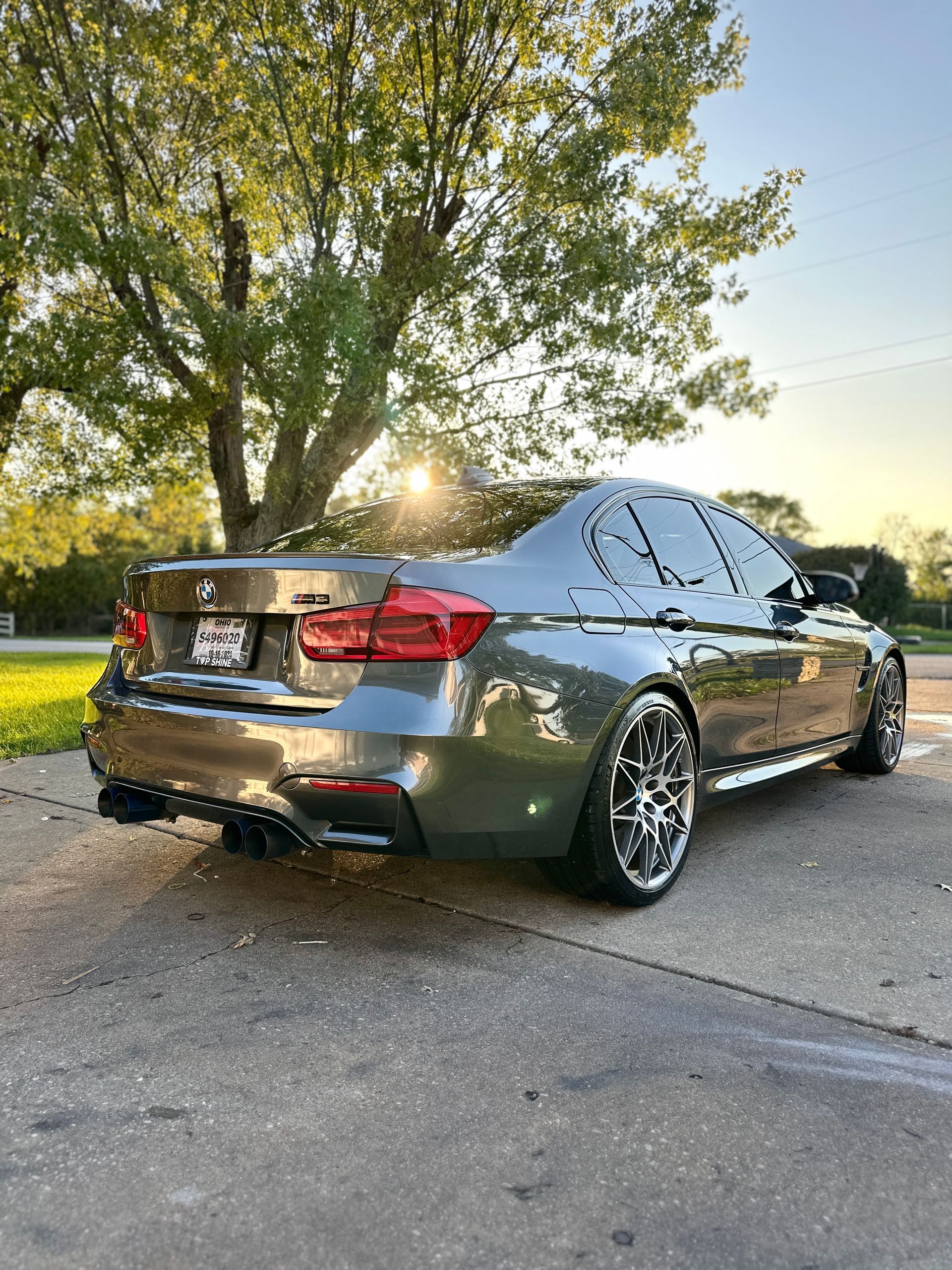 Gray BMW sedan parked on a driveway, chrome wheels, dark tinted windows, sunlight in background.