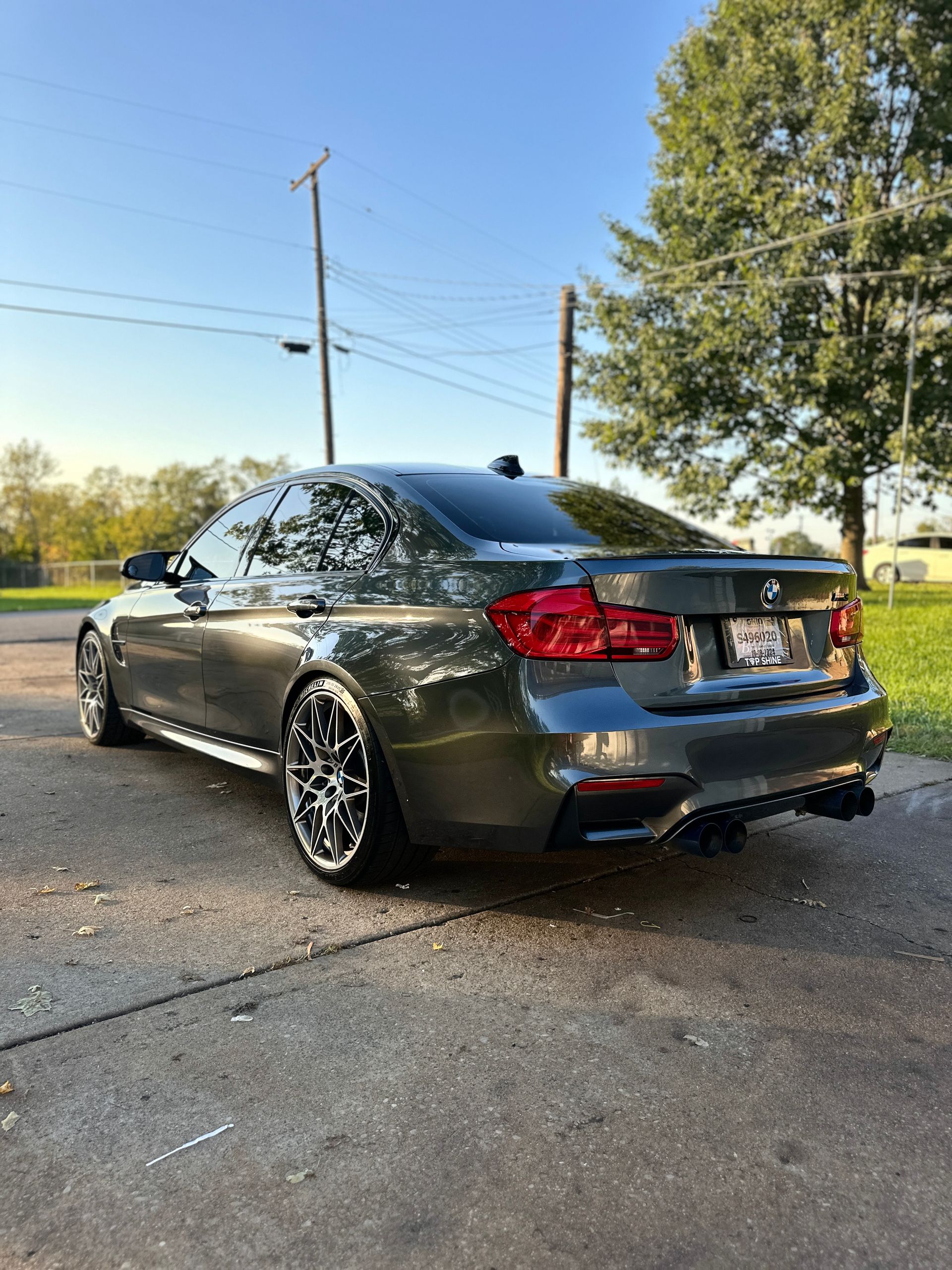 Gray BMW sedan parked on a driveway with custom wheels and a black diffuser; sunny day.